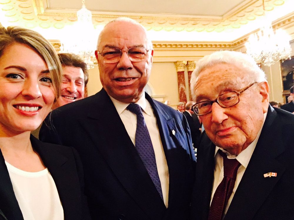 Mélanie Joly standing between Colin Powell and Henry Kissinger at a State Department lunch. Kissinger is wearing a Canadian flag pin.